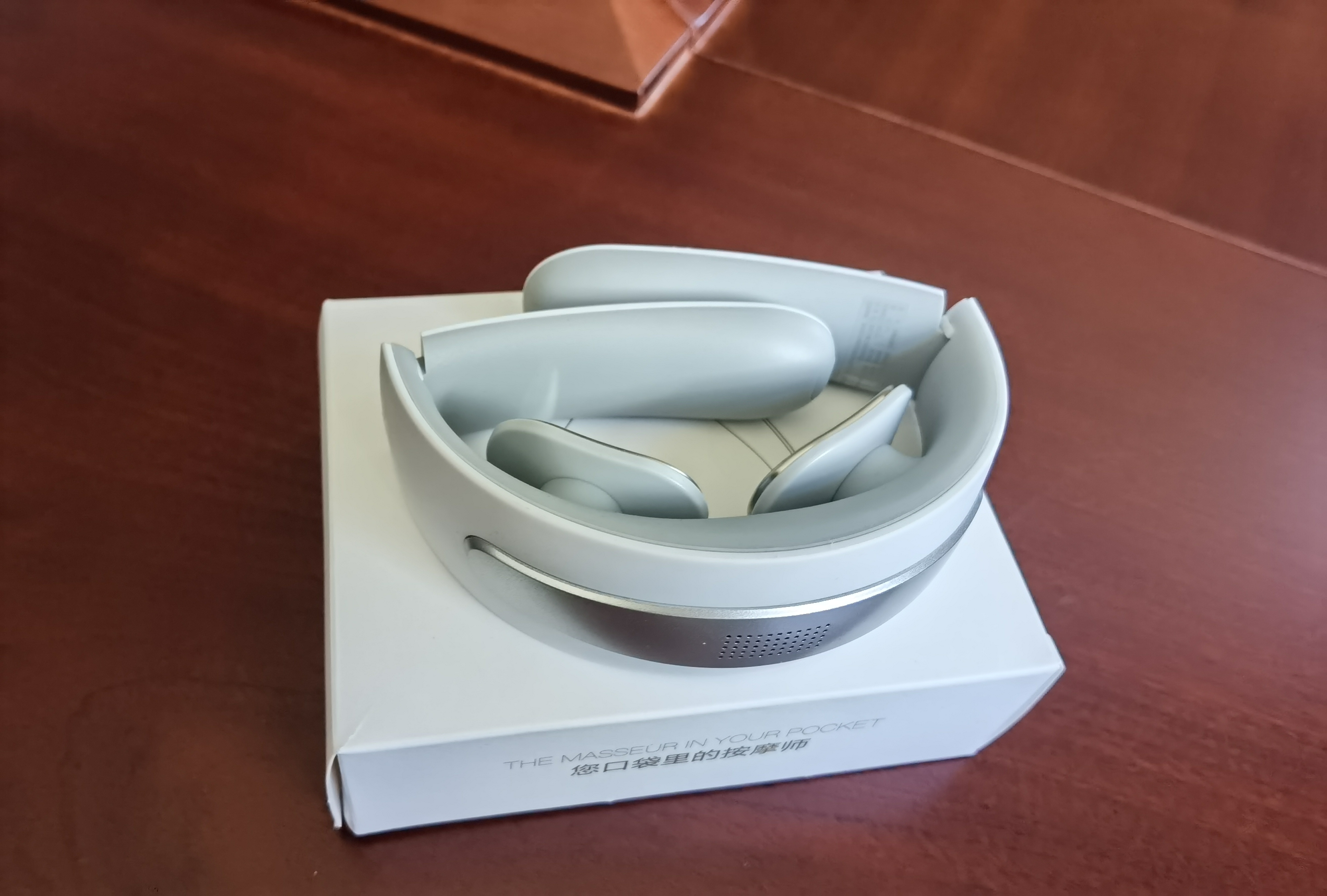 Photograph of a Meilan F5 foldable neck massager sample resting folded on its box